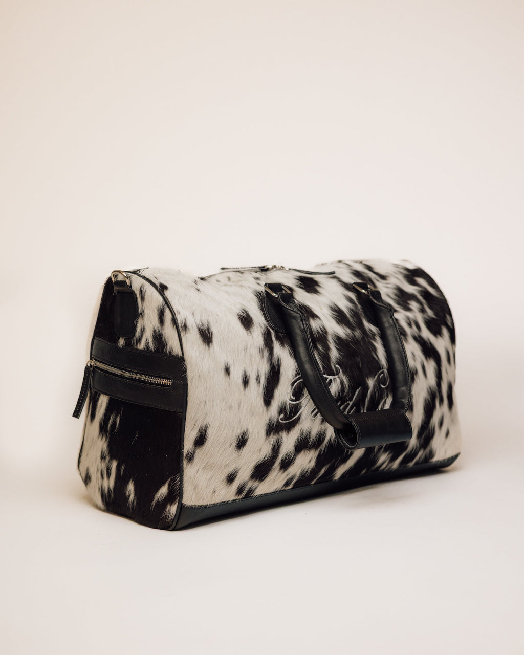 Black and white cowhide duffle carried by shoulder strap