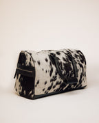 Black and white cowhide duffle carried by shoulder strap
