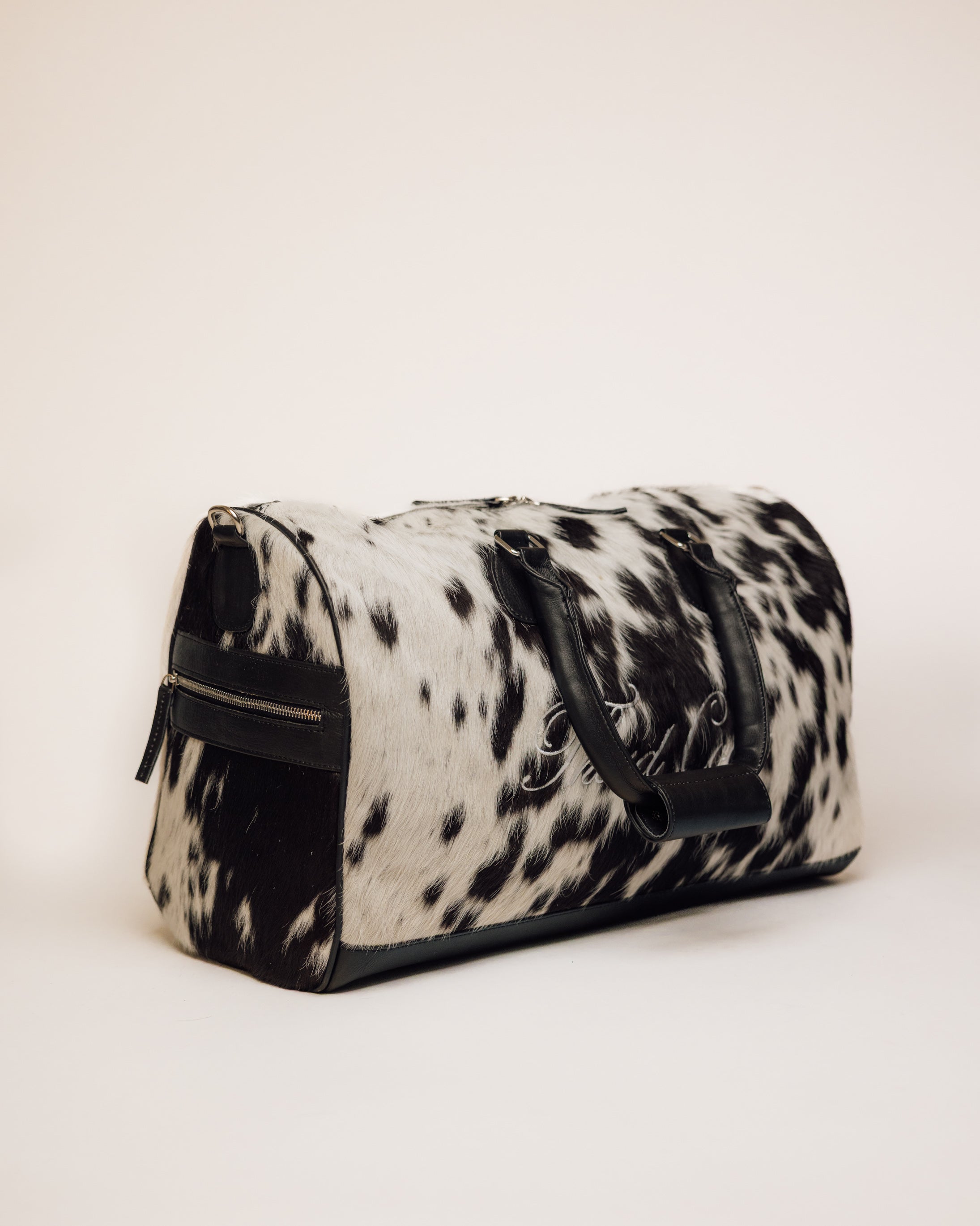 Black and white cowhide duffle carried by shoulder strap