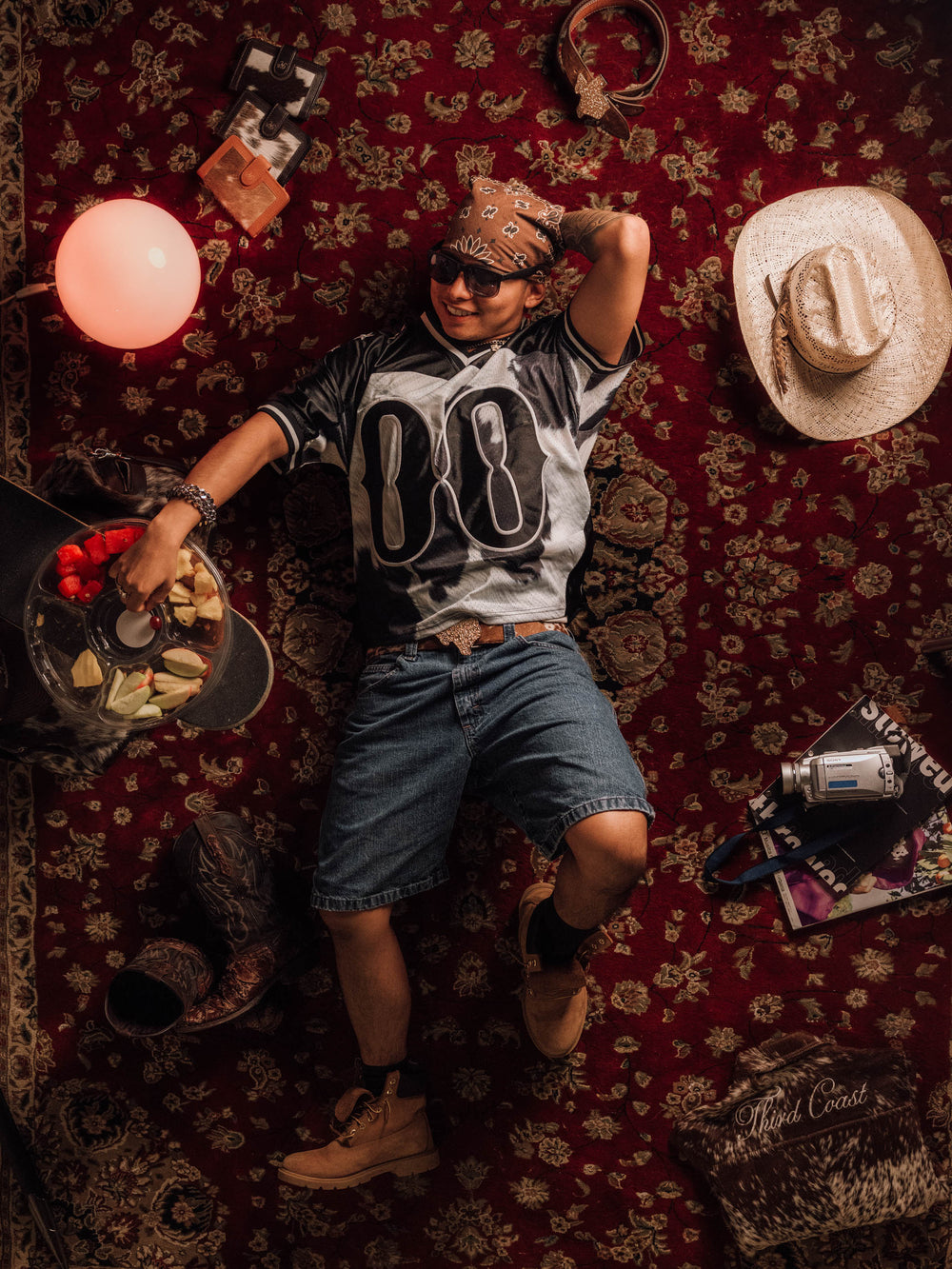 The Legacy jersey with jean shorts and a bandana, laid out on a red rug with cowboy hats and boots