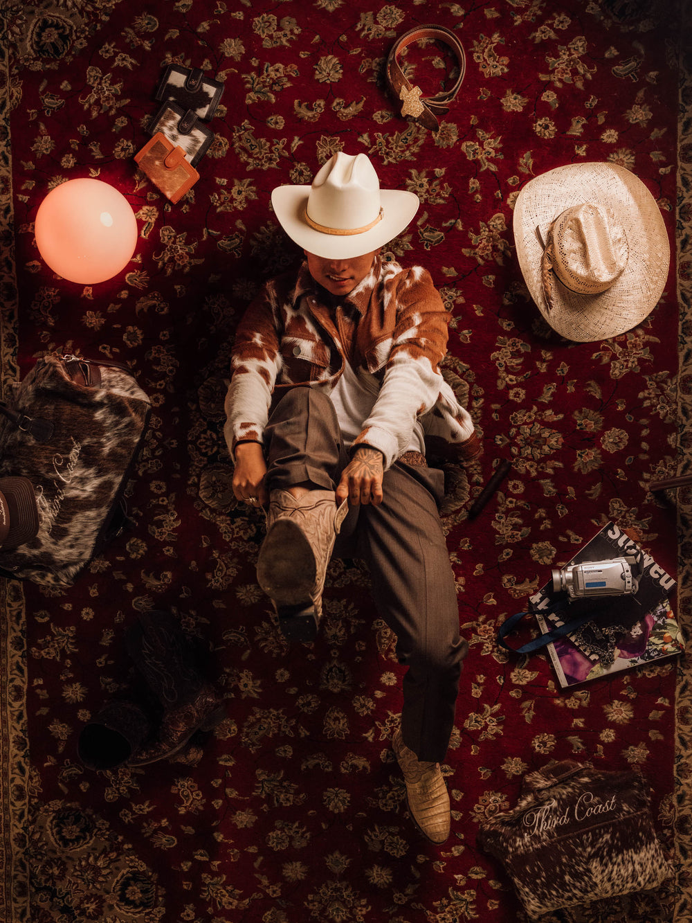 Red Angus cowhide jacket with a white cowboy hat, brown pants and boots, on a red rug