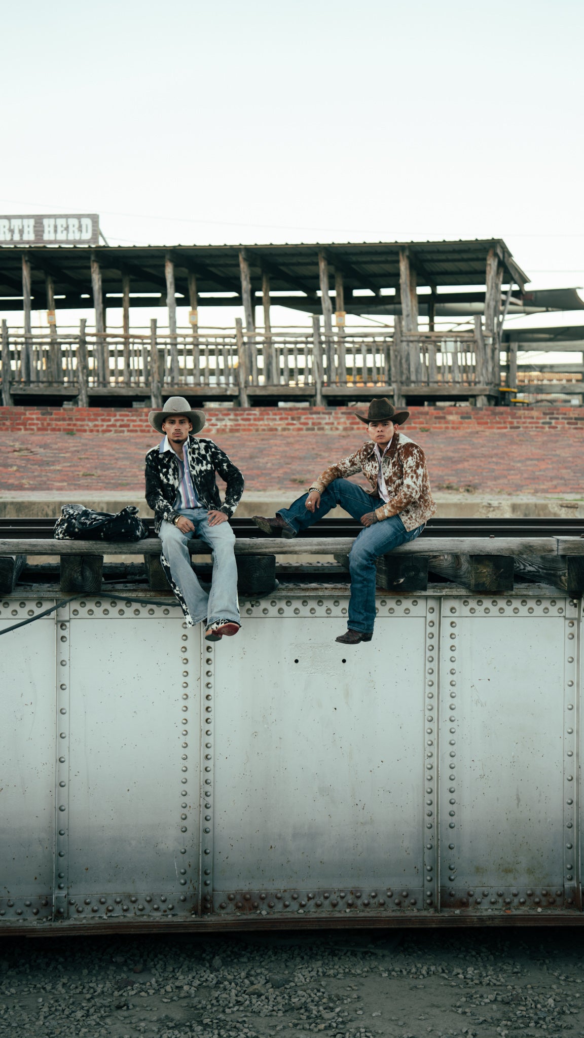 Andy and Gera sitting on a rail at the stockyards in cowboy hats and cowhide